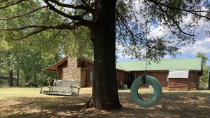 A rustic cabin with a stone chimney, a swing, and a tire swing hanging from a tree.