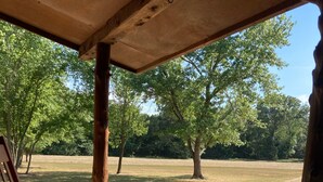 A wooden bench under a covered area with a view of a grassy field and trees.