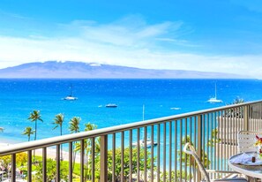 A balcony with a view of the ocean, palm trees, and a mountainous landscape.