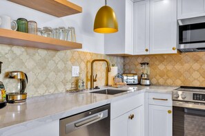 A modern kitchen with white cabinets, a stainless steel dishwasher, a coffee maker, a toaster, and a blender.