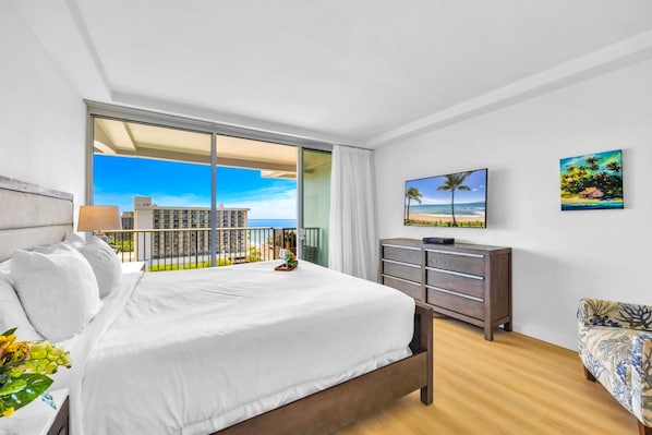 A hotel room with a bed, a dresser, a TV, and a balcony with a view of the ocean.