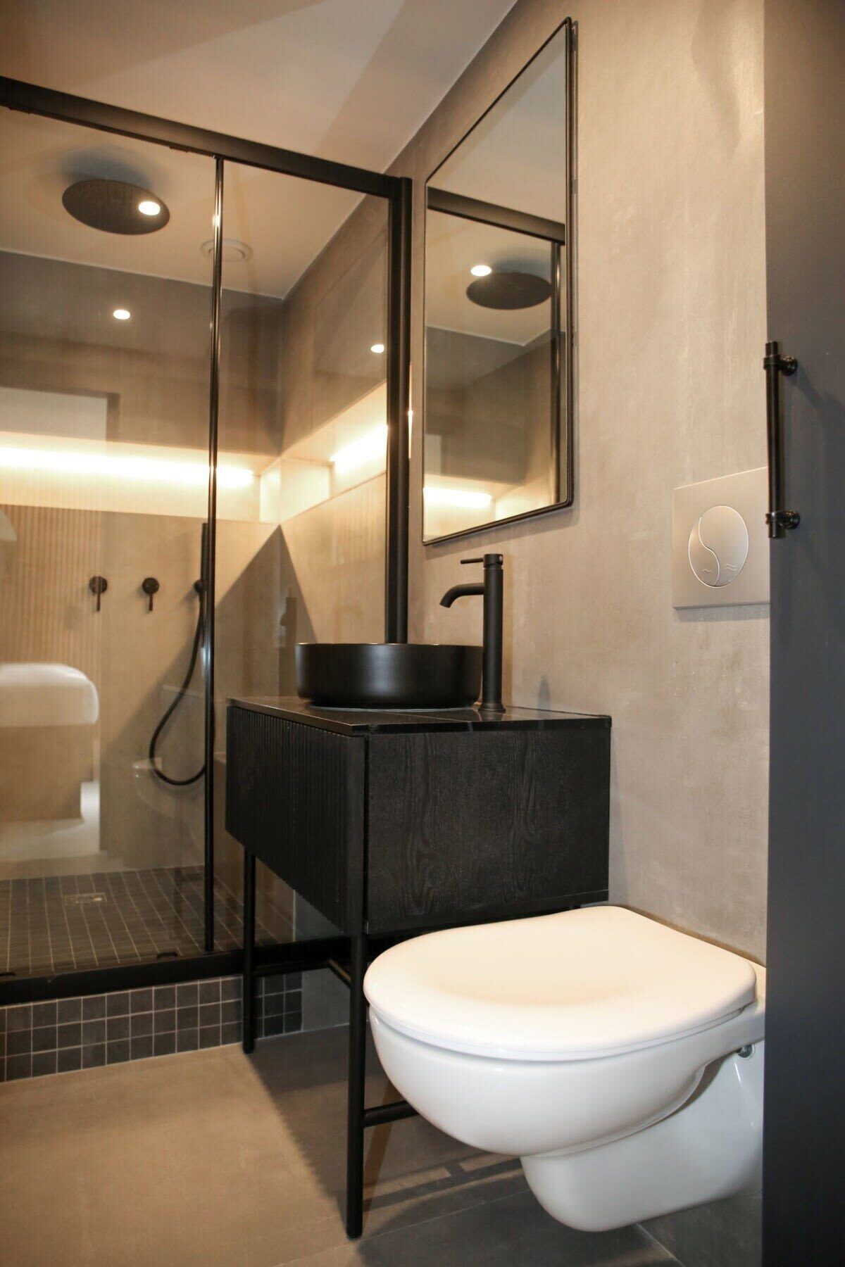 Een moderne badkamer met een glazen douchecabine, een zwarte wastafel en een wit toilet.