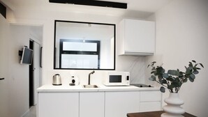 Una cocina compacta con armarios blancos, un microondas, un hervidor y un lavabo.