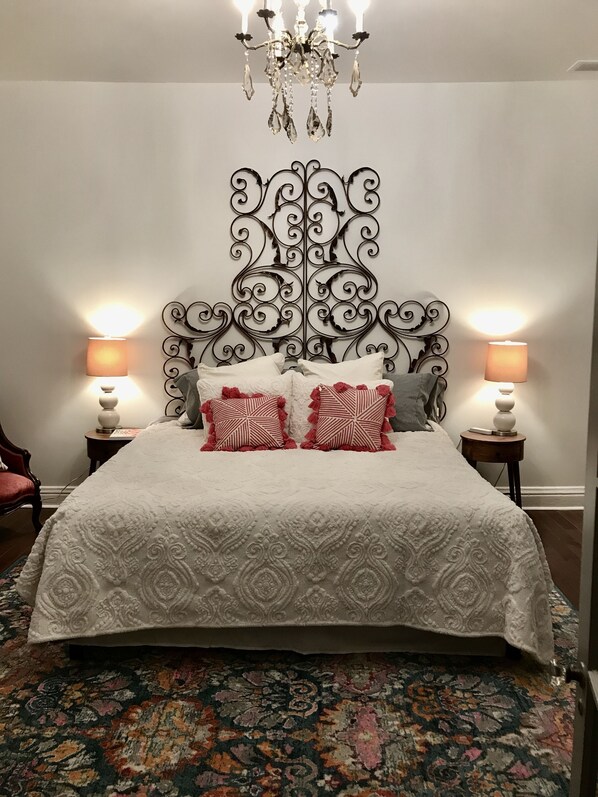 A bedroom with a large bed, ornate headboard, two bedside lamps, and a chandelier.