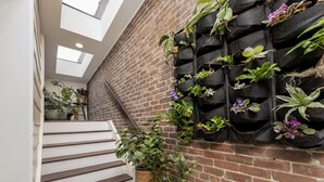 Un escalier, avec un mur de briques d’un côté et un mur-jardinière noir de l’autre, où sont plantées différentes espèces de plantes et de fleurs.