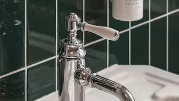 A bathroom with a chrome faucet, a white sink, and a bottle of hand soap on the wall.