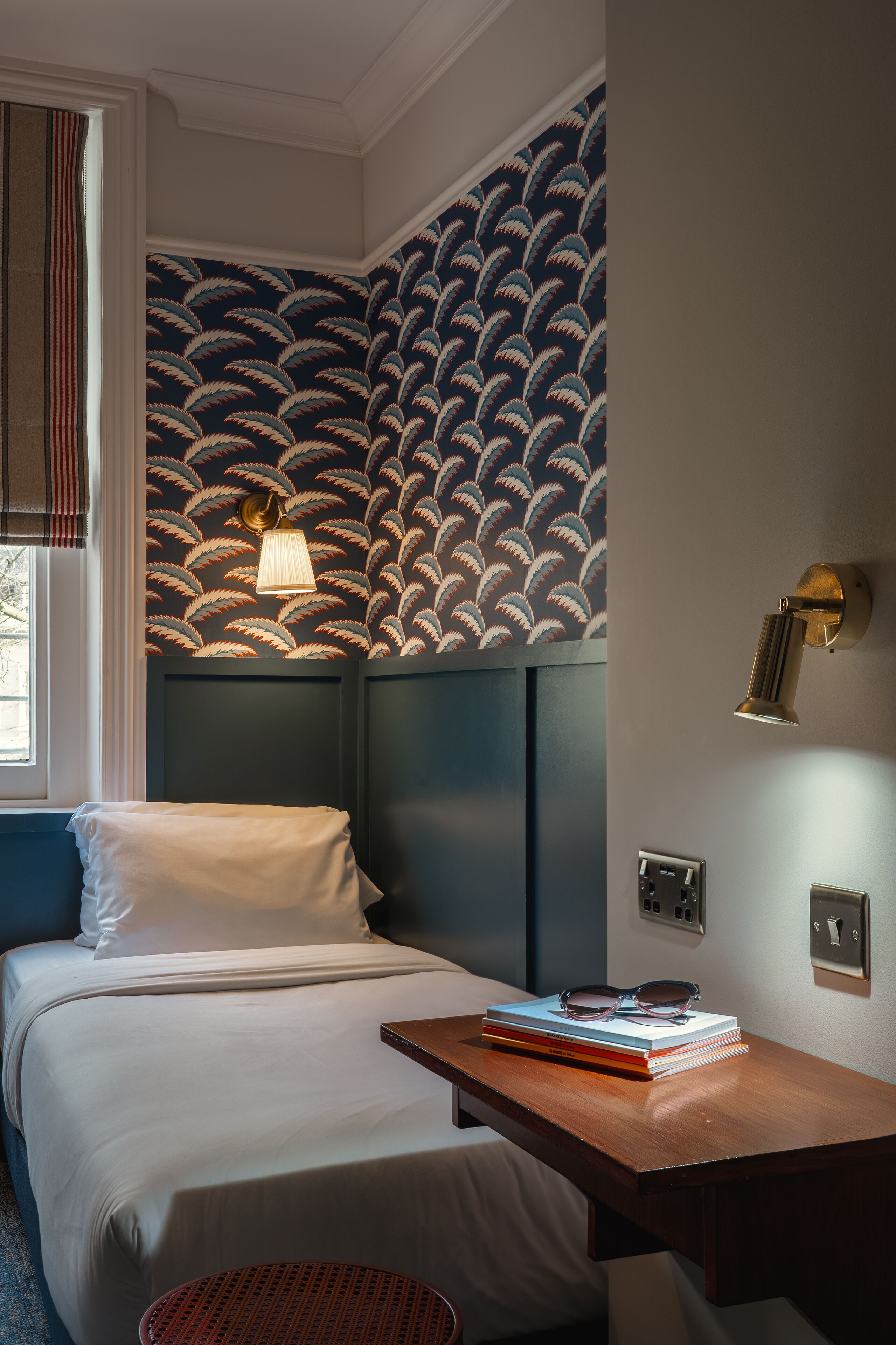 Quarto de hotel com uma cama, uma mesa de trabalho e um papel de parede estampado.