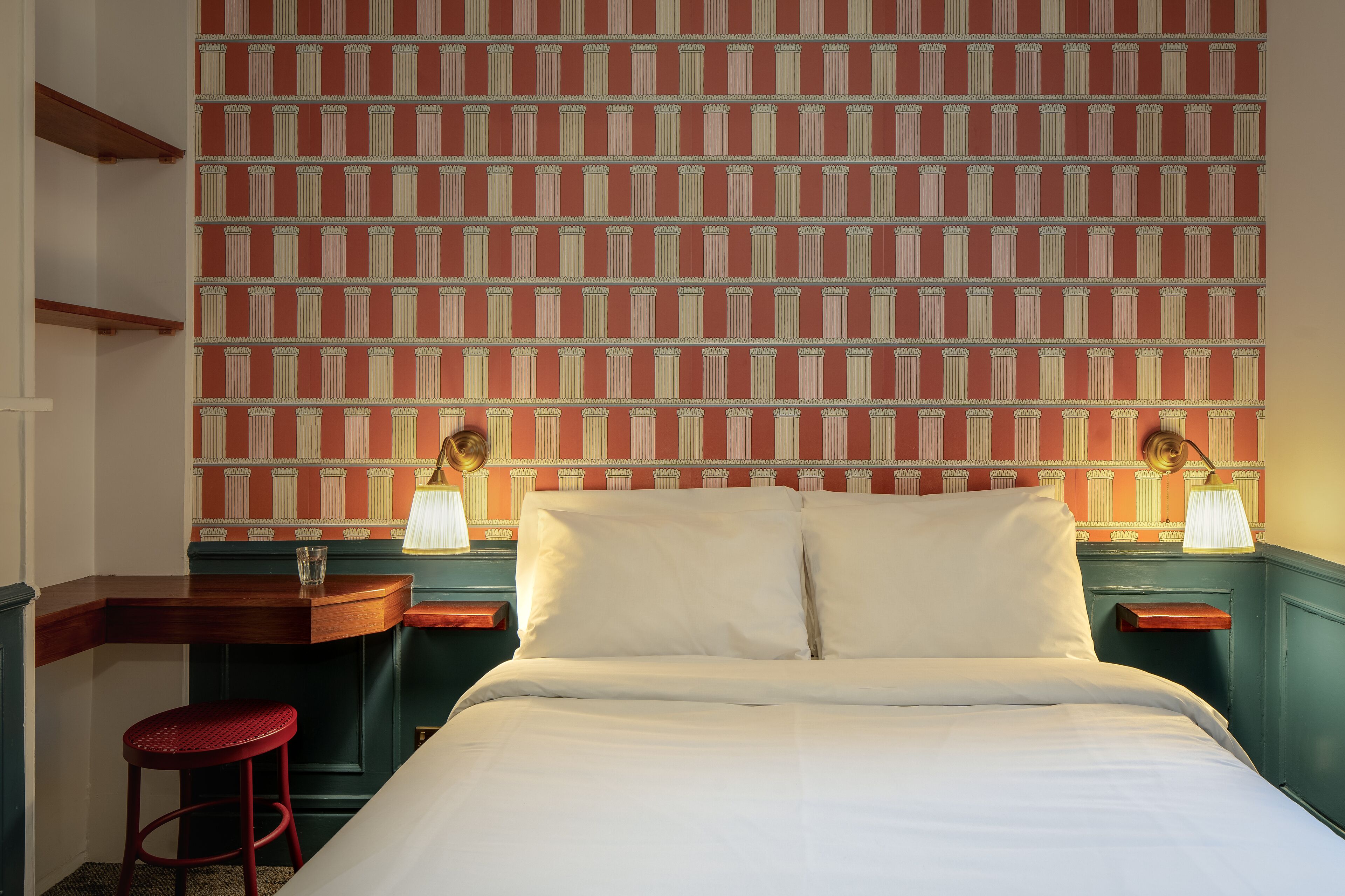 A hotel room with a bed, two nightstands, a desk, and a red chair.