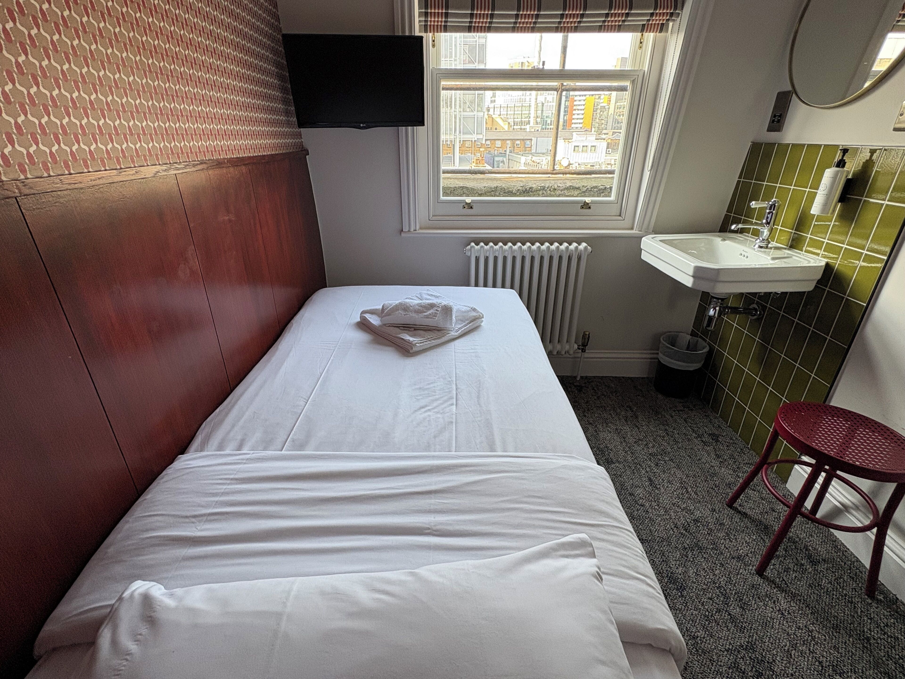 A hotel room with a bed, a window, a radiator, a sink, and a red chair.