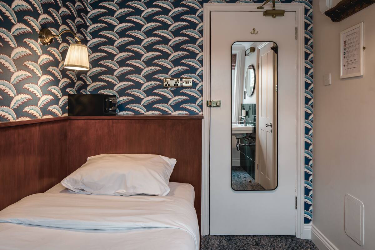 A bedroom with a bed, a nightstand, a mirror, and a patterned wallpaper.