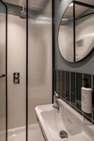 Ein modernes Badezimmer mit einer gläsernen Dusche, einem großen Spiegel und einem weißen Waschbecken.