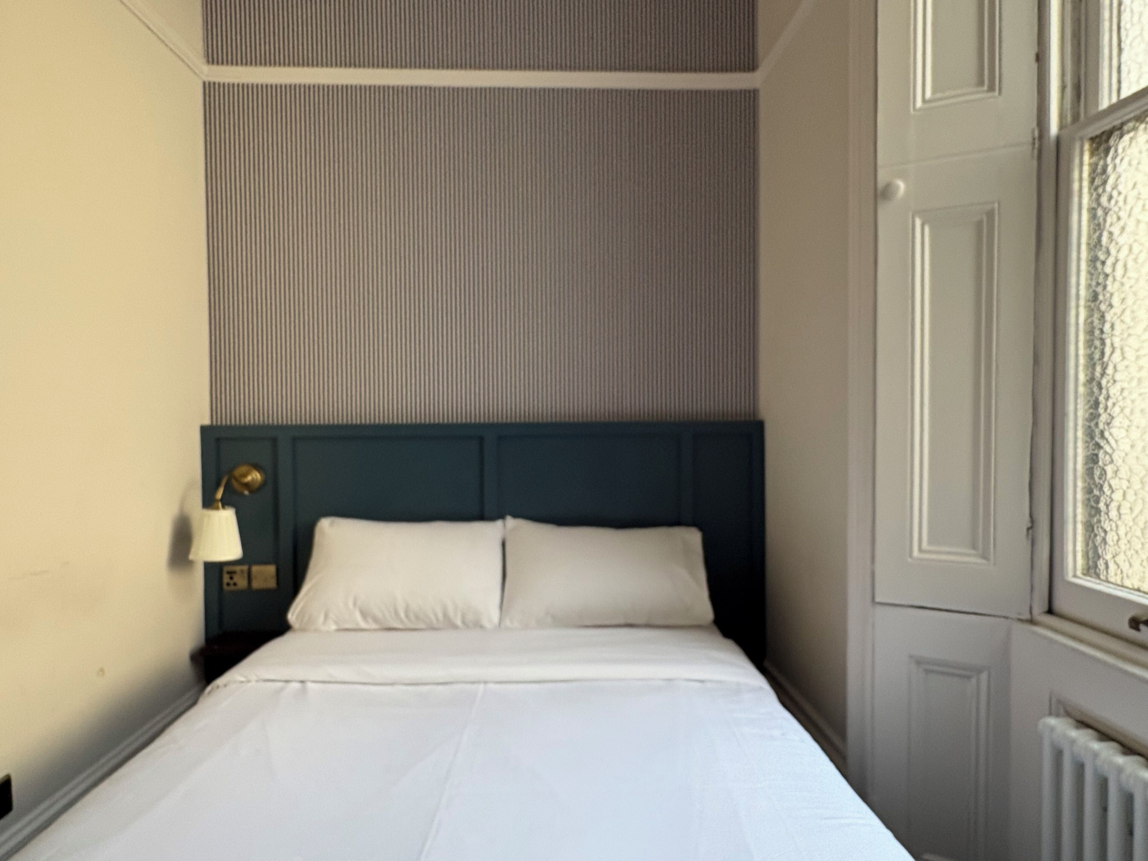 Une chambre d’hôtel avec un lit, une table de chevet, une lampe et une fenêtre.