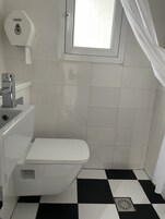 Casa de banho com sanita, secador de mãos e janela com cortina.