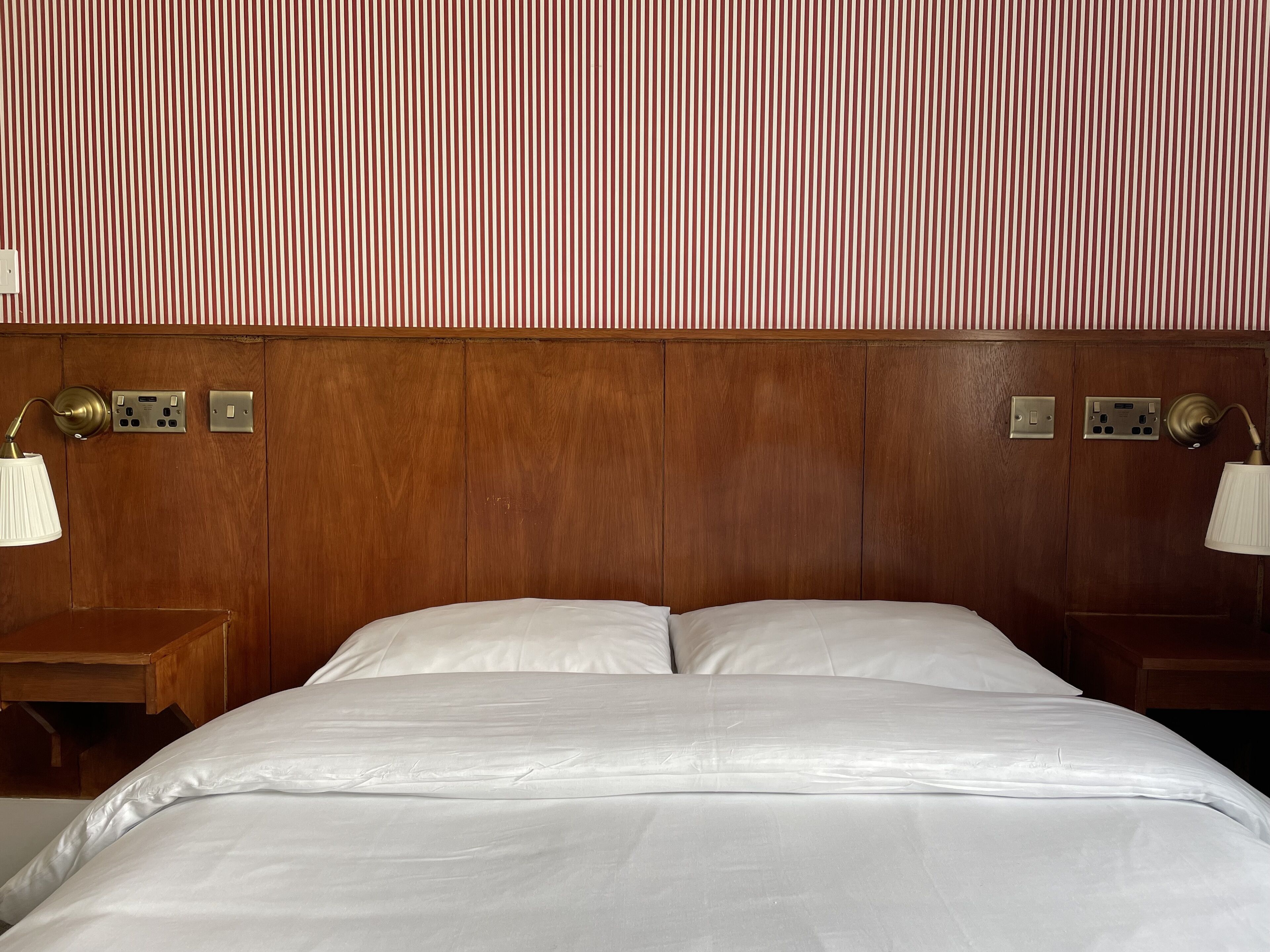 A hotel room with a wooden headboard, two bedside tables with lamps, and a bed with white linens.
