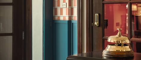 A hotel lobby with a wooden reception desk, a blue door, and a red wall with a patterned design.