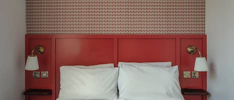 Una cama con sábanas blancas, un cabecero rojo y dos lámparas de noche.
