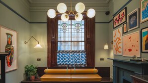 Un coin salon accueillant avec un banc et une table, une fenêtre décorative avec des vitraux, et divers tableaux encadrés accrochés aux murs.