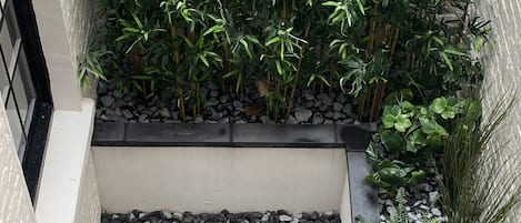 A courtyard with a patterned tile floor, surrounded by plants and a stone border.
