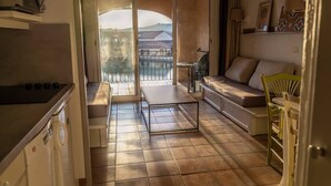A compact living space with a kitchenette, a sofa, a dining table, and a view of a balcony with a railing. - Magnificent lake view at Golf de Pont-Royal (Mallemort)