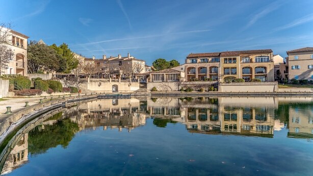 A serene water body reflecting buildings with arched windows and a clear sky. - Magnificent lake view at Golf de Pont-Royal (Mallemort)