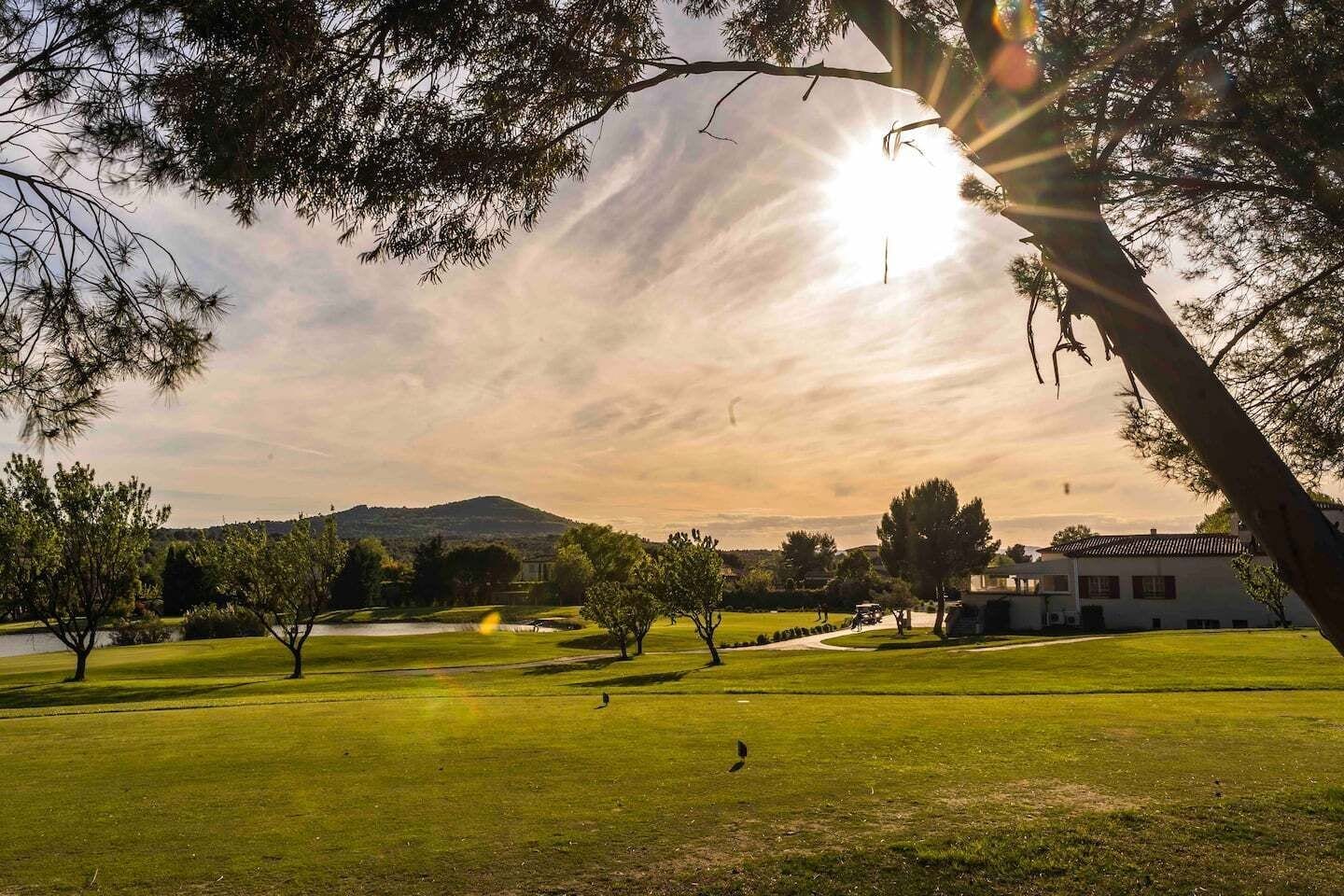 A golf course with a clubhouse, trees, and a mountain in the background.