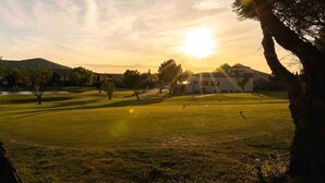 A golf course with a clubhouse, trees, and a sunset in the background. - Magnificent lake view at Golf de Pont-Royal (Mallemort)