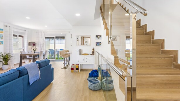 A modern living room with a blue sofa, a wooden staircase, and a dining area.