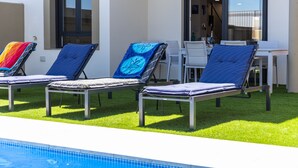 A poolside area with lounge chairs and a table, surrounded by a well-maintained lawn.