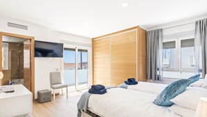 A modern hotel room with a large bed, a TV, a desk, and a sliding door to a balcony.