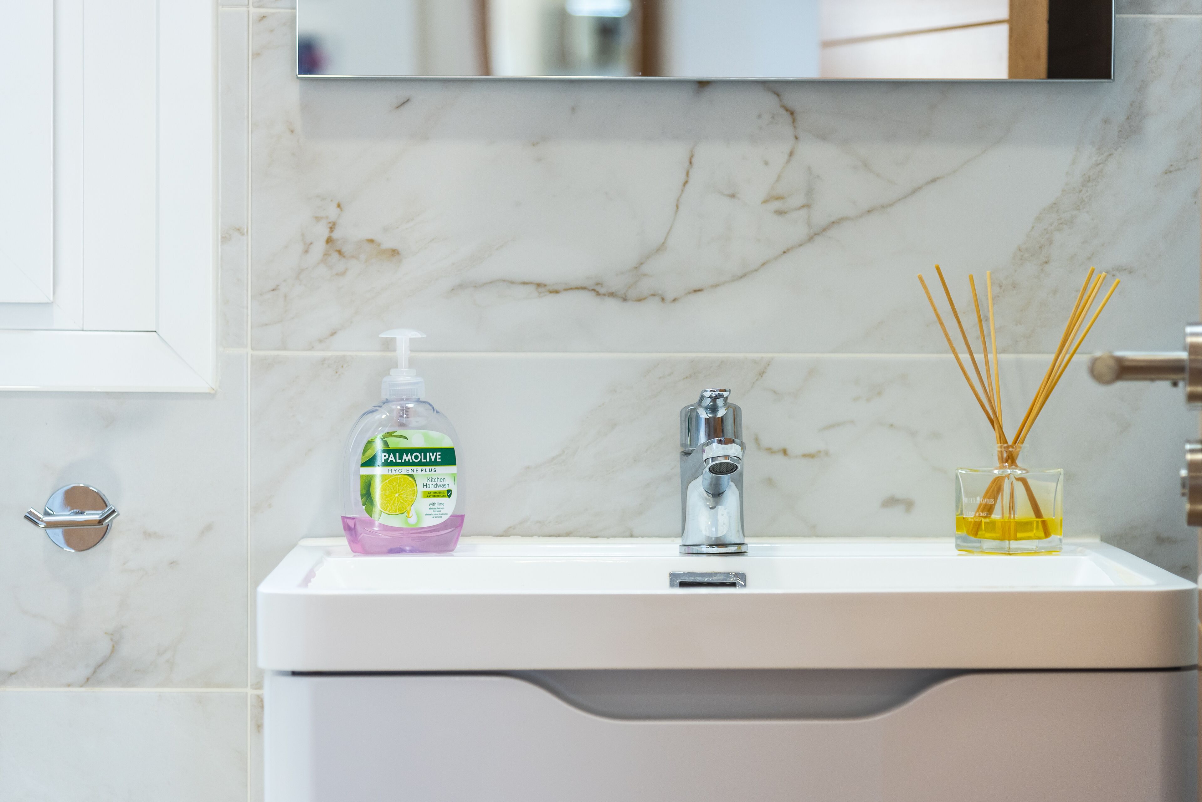 A bathroom sink with a marble backsplash, a soap dispenser, a faucet, and reed diffuser.
