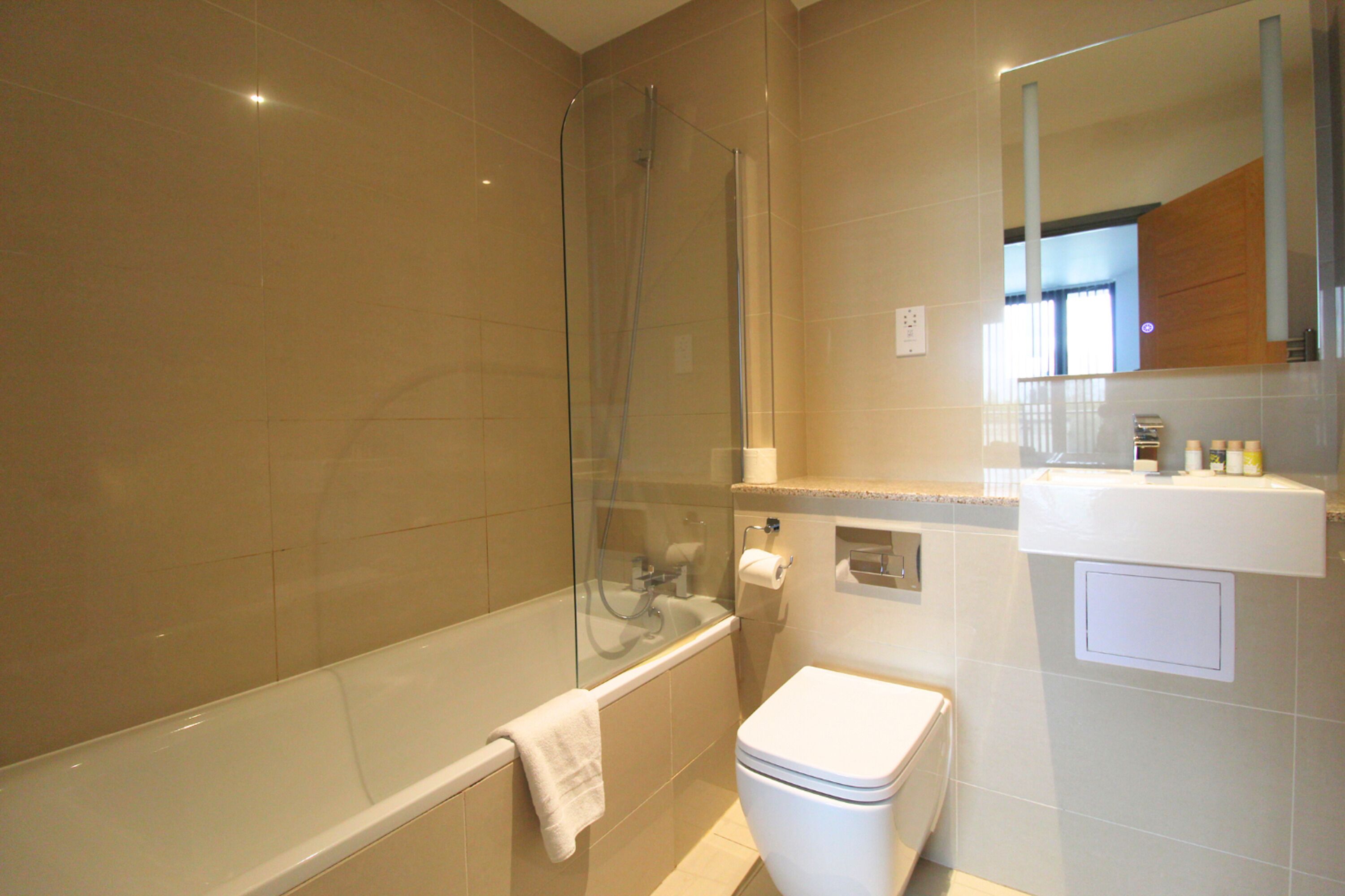 Un baño moderno con cabina de ducha de vidrio, inodoro blanco y lavamanos con artículos de aseo.