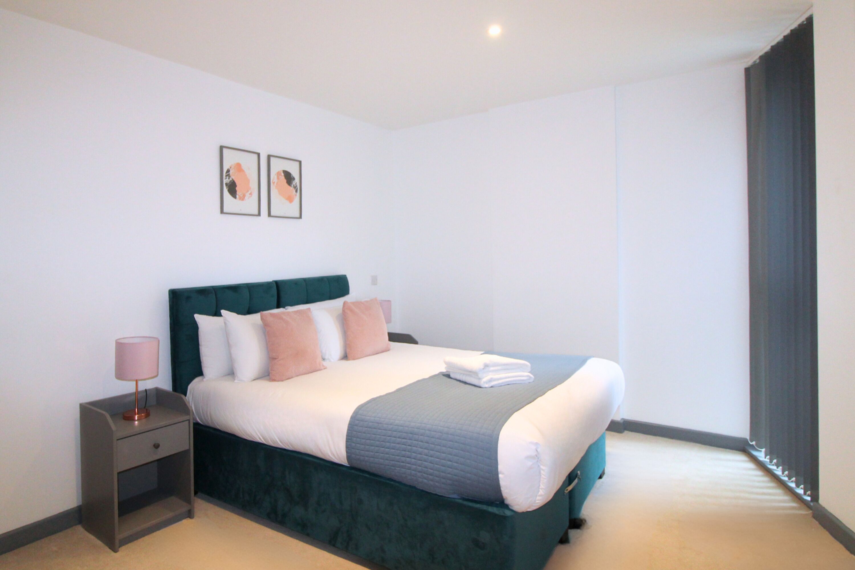 A neatly made bed with a green headboard, a bedside table with a lamp, and two framed pictures on the wall.
