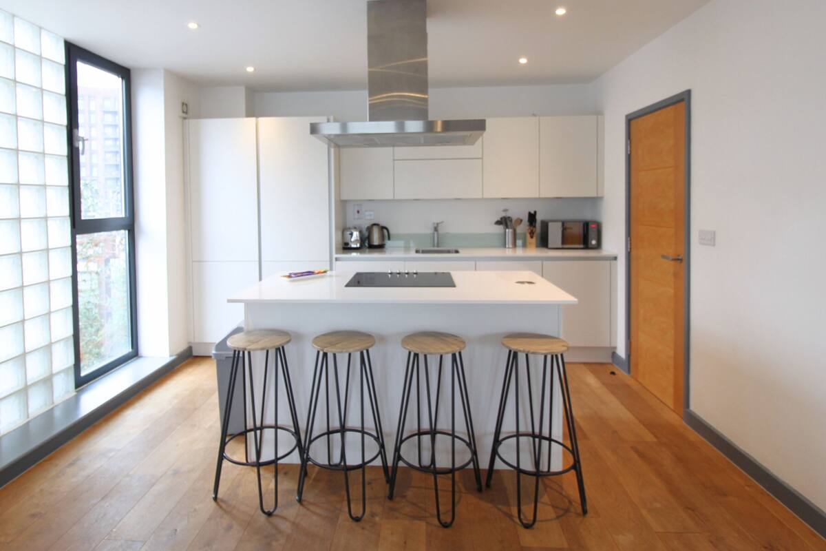 A modern kitchen with a central island, bar stools, and a large window.