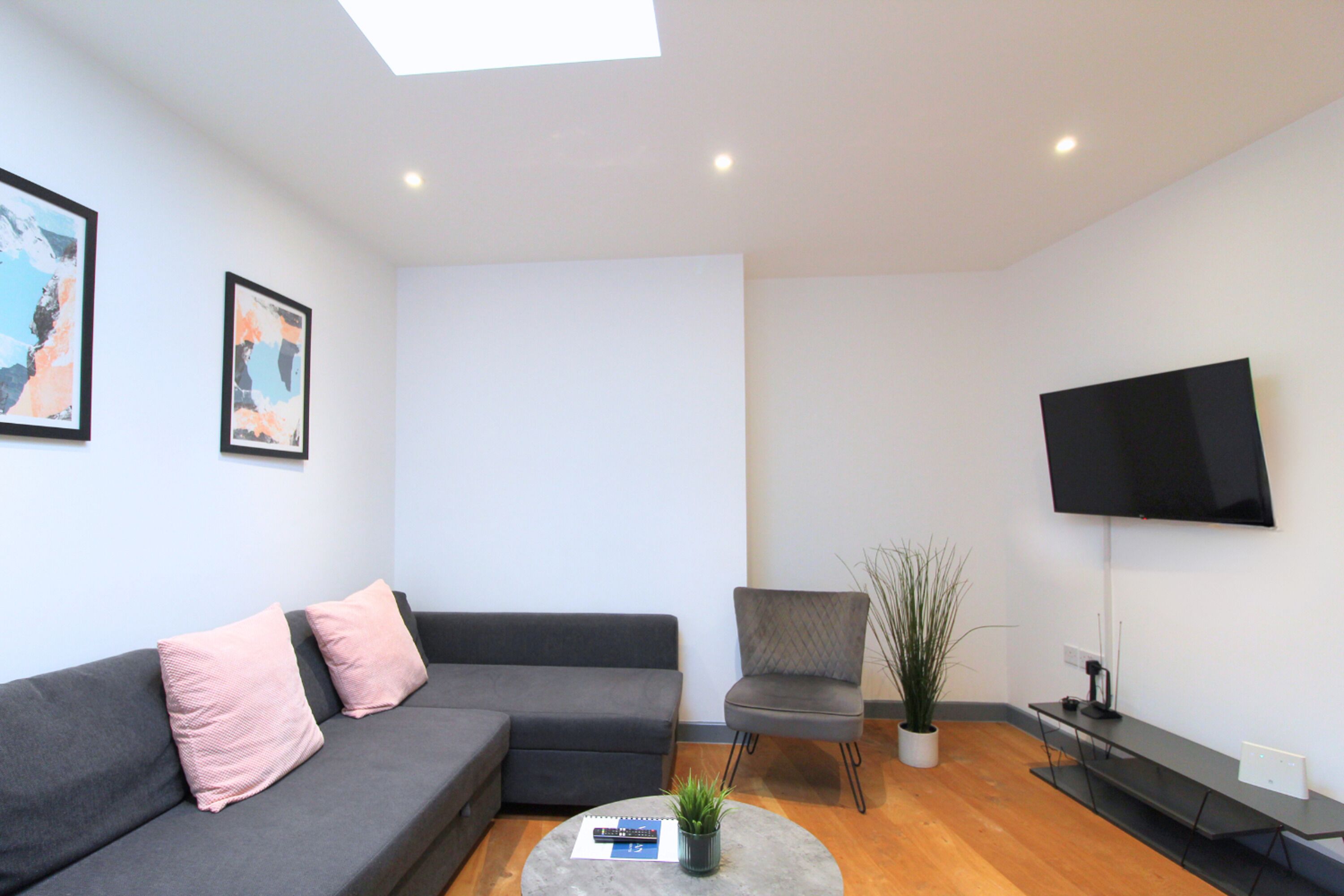 A modern living room with a grey sofa, a small round coffee table, a grey armchair, a potted plant, and a flat-screen TV mounted on the wall.