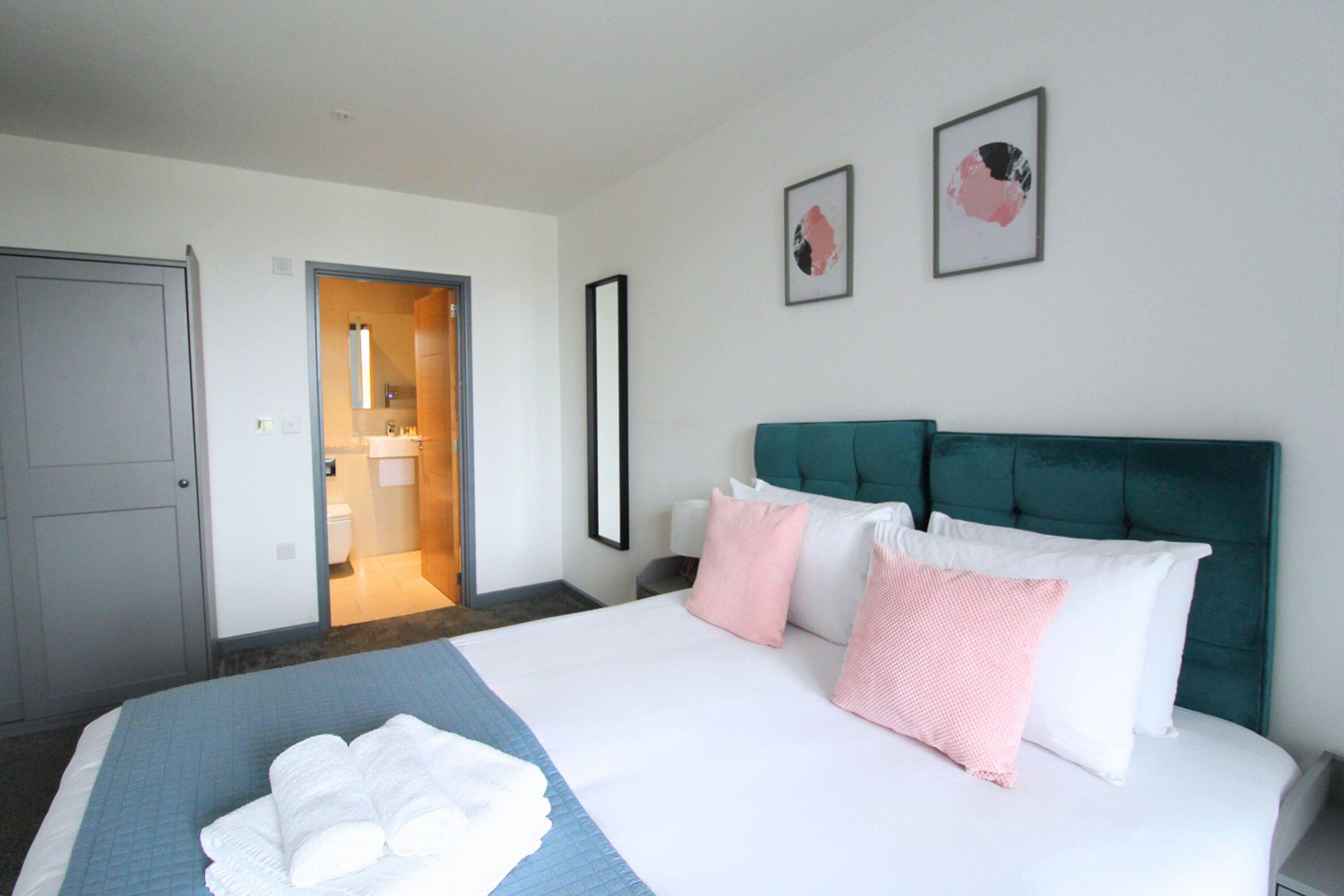 A hotel room with a bed, a bathroom visible through an open door, and two framed pictures on the wall.