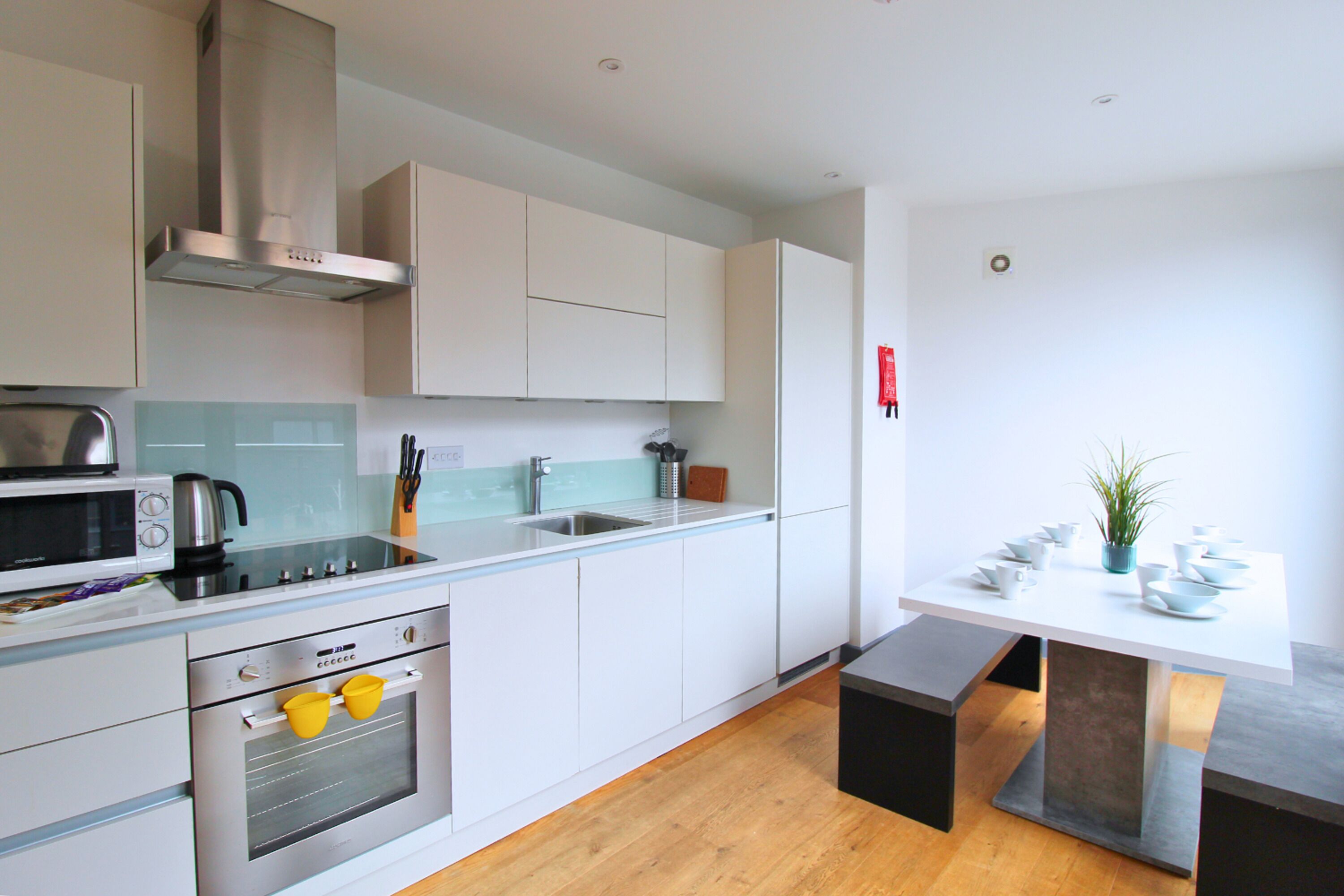 Una cocina moderna con armarios blancos, un horno de acero inoxidable, un microondas y un lavabo.