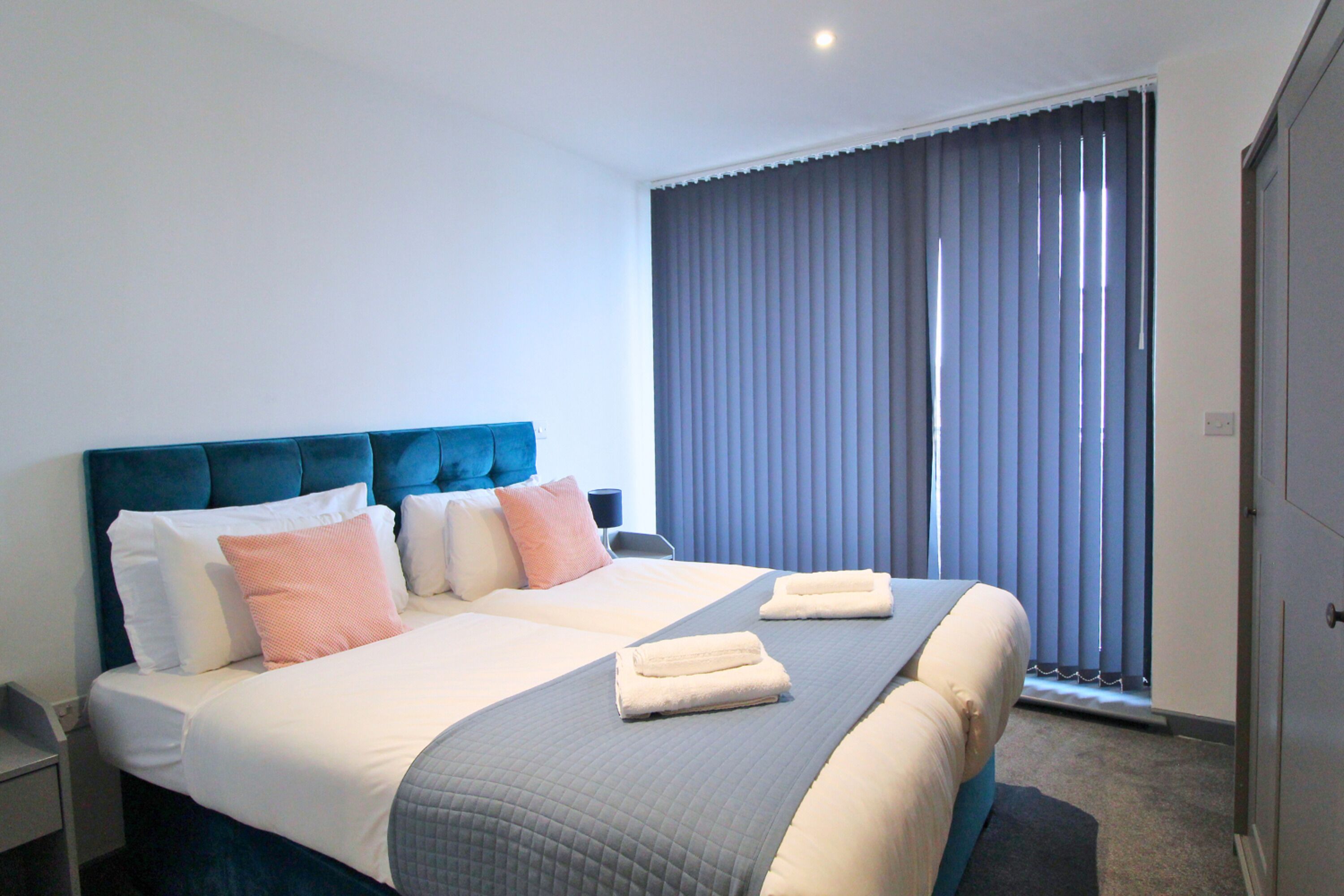 A hotel room with a large bed, a headboard, and a window with blinds.