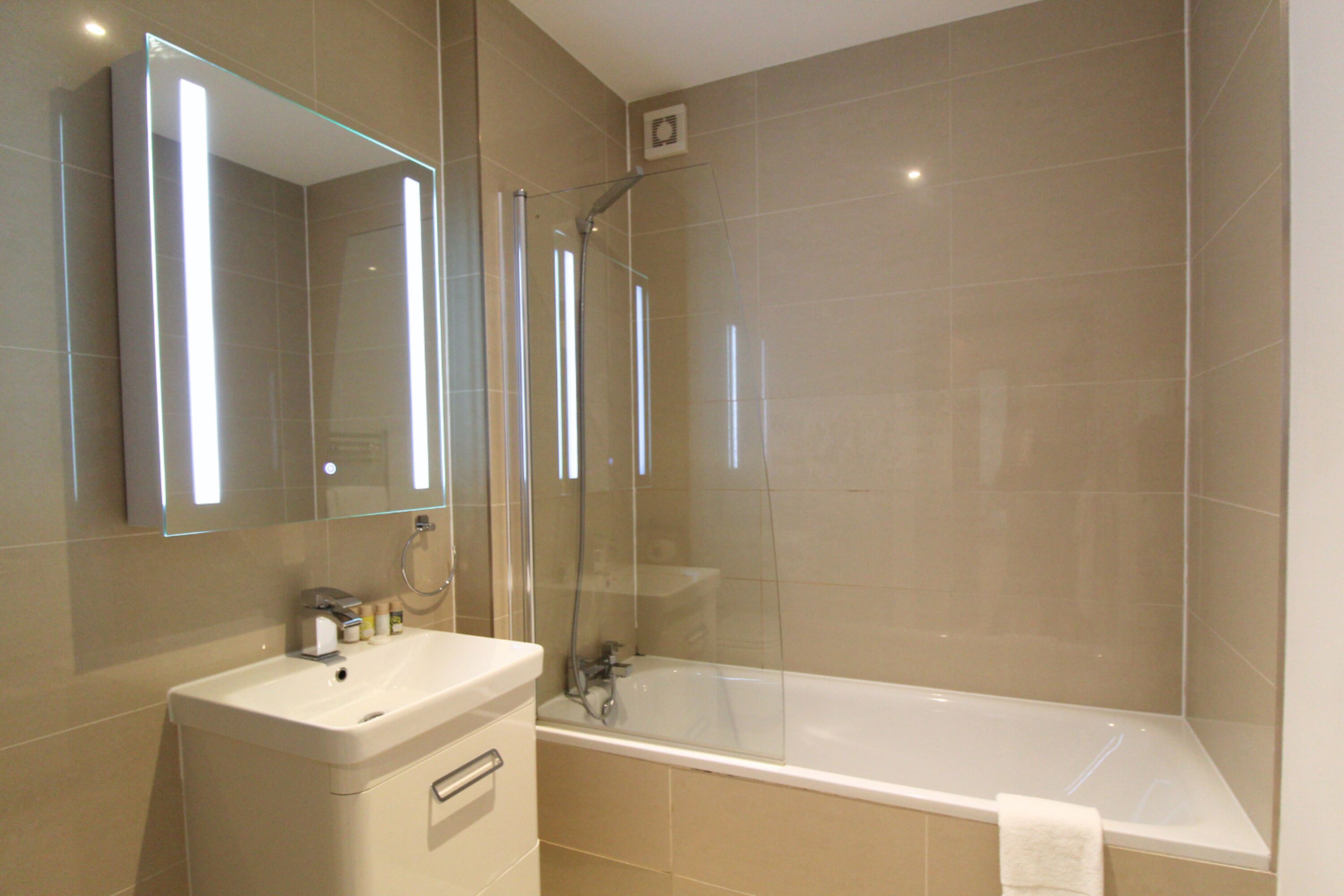 Un baño moderno con ducha de vidrio, lavamanos blanco y un espejo grande.