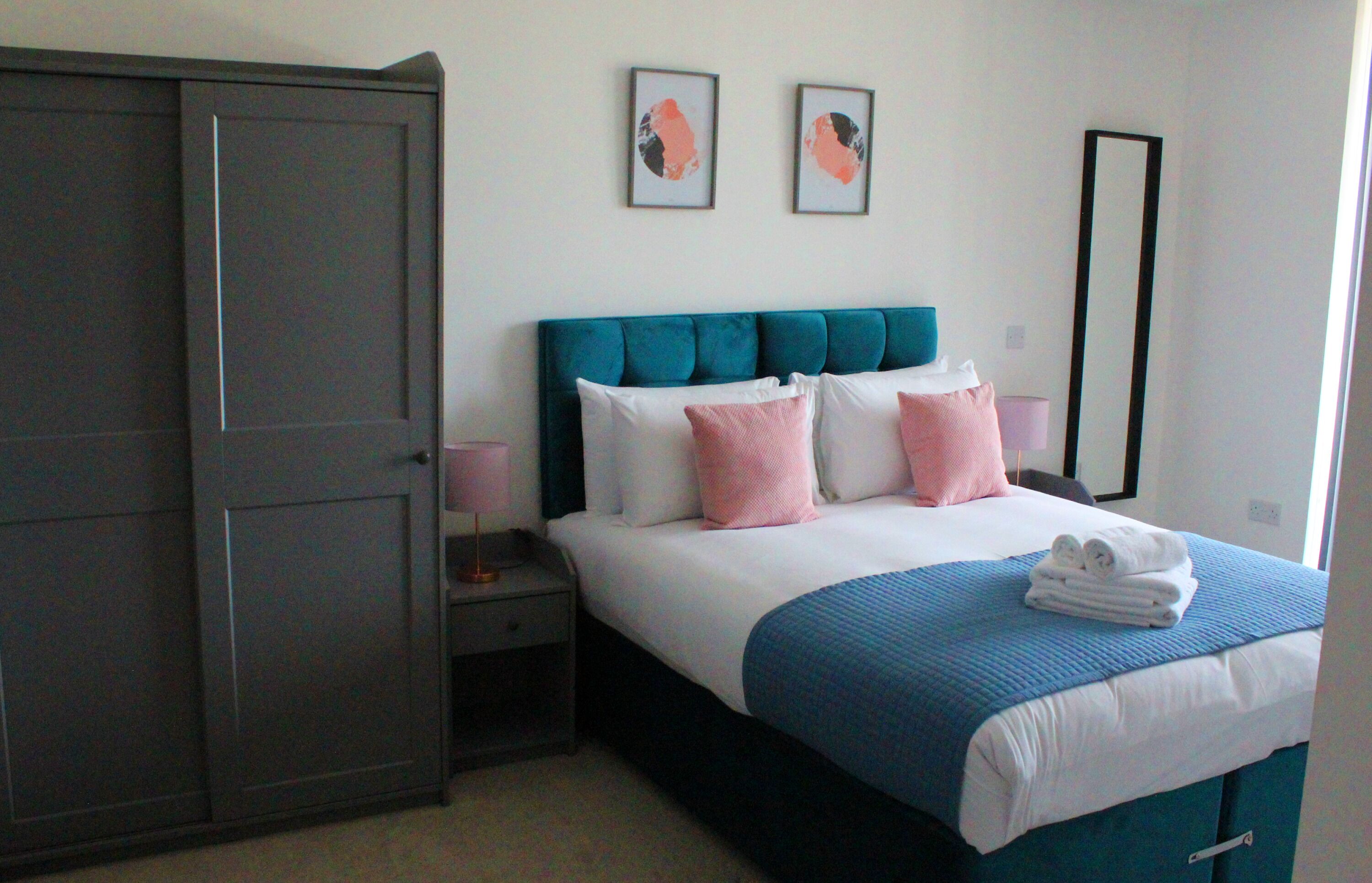 A bedroom with a bed, a wardrobe, a nightstand, and two framed pictures on the wall.