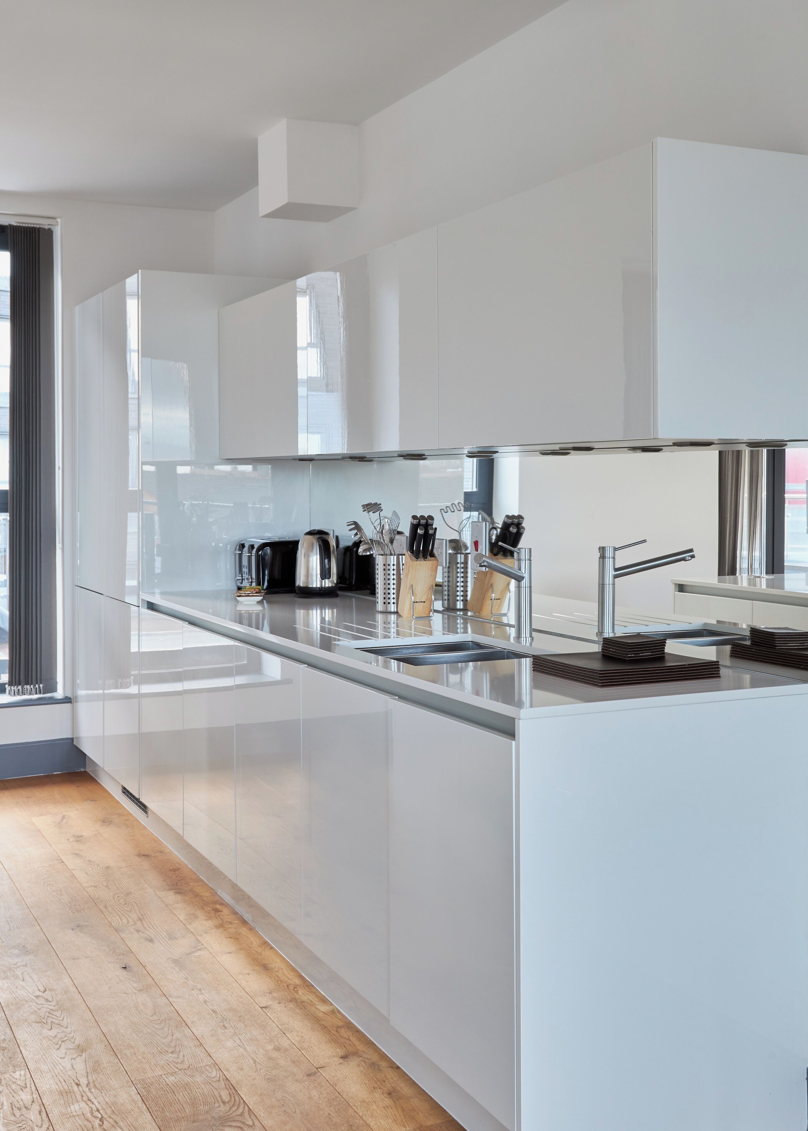 A modern kitchen with white cabinetry, a stainless steel sink, and a wooden floor.