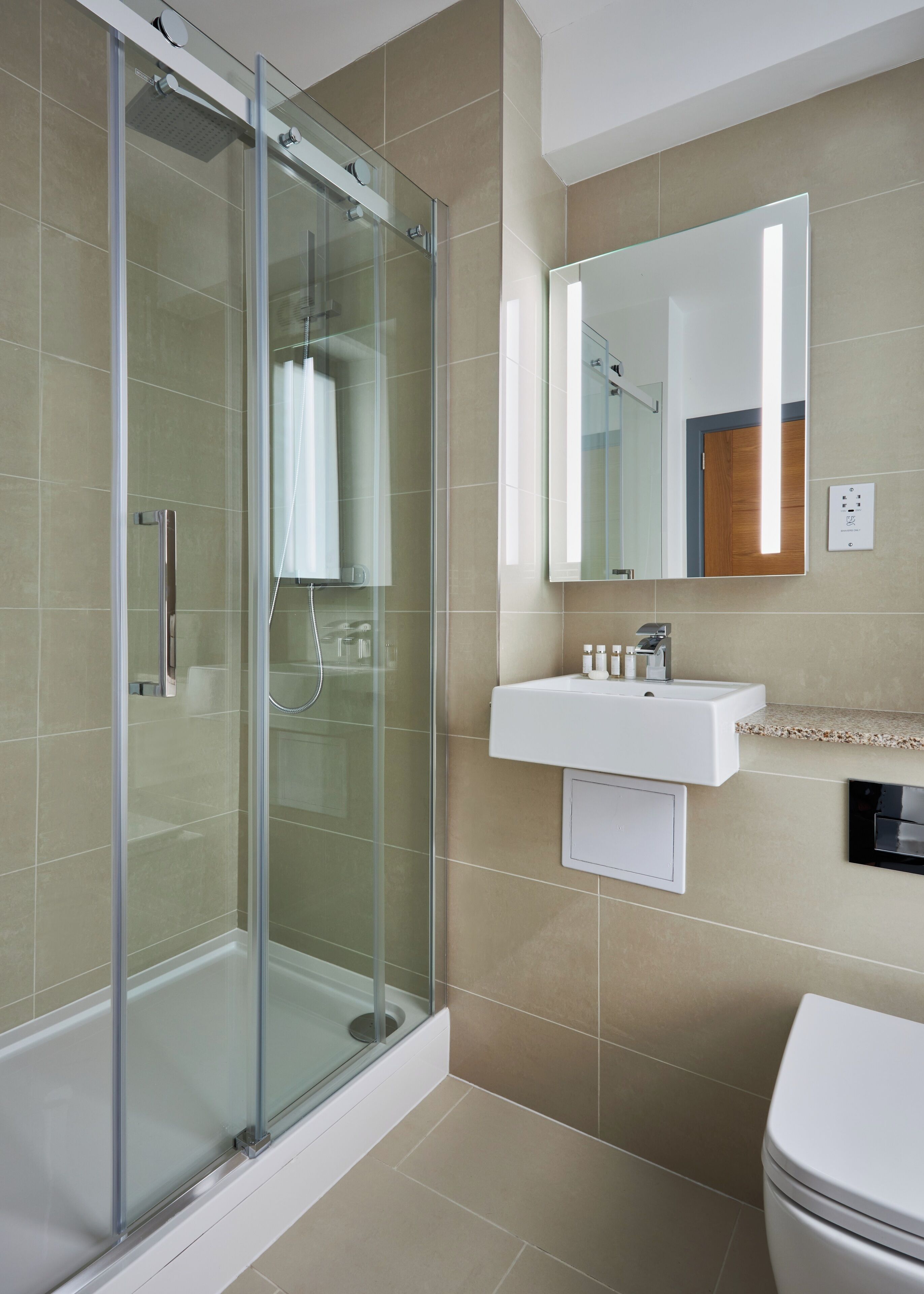 A modern bathroom with a glass-enclosed shower, a white sink, and a large mirror.