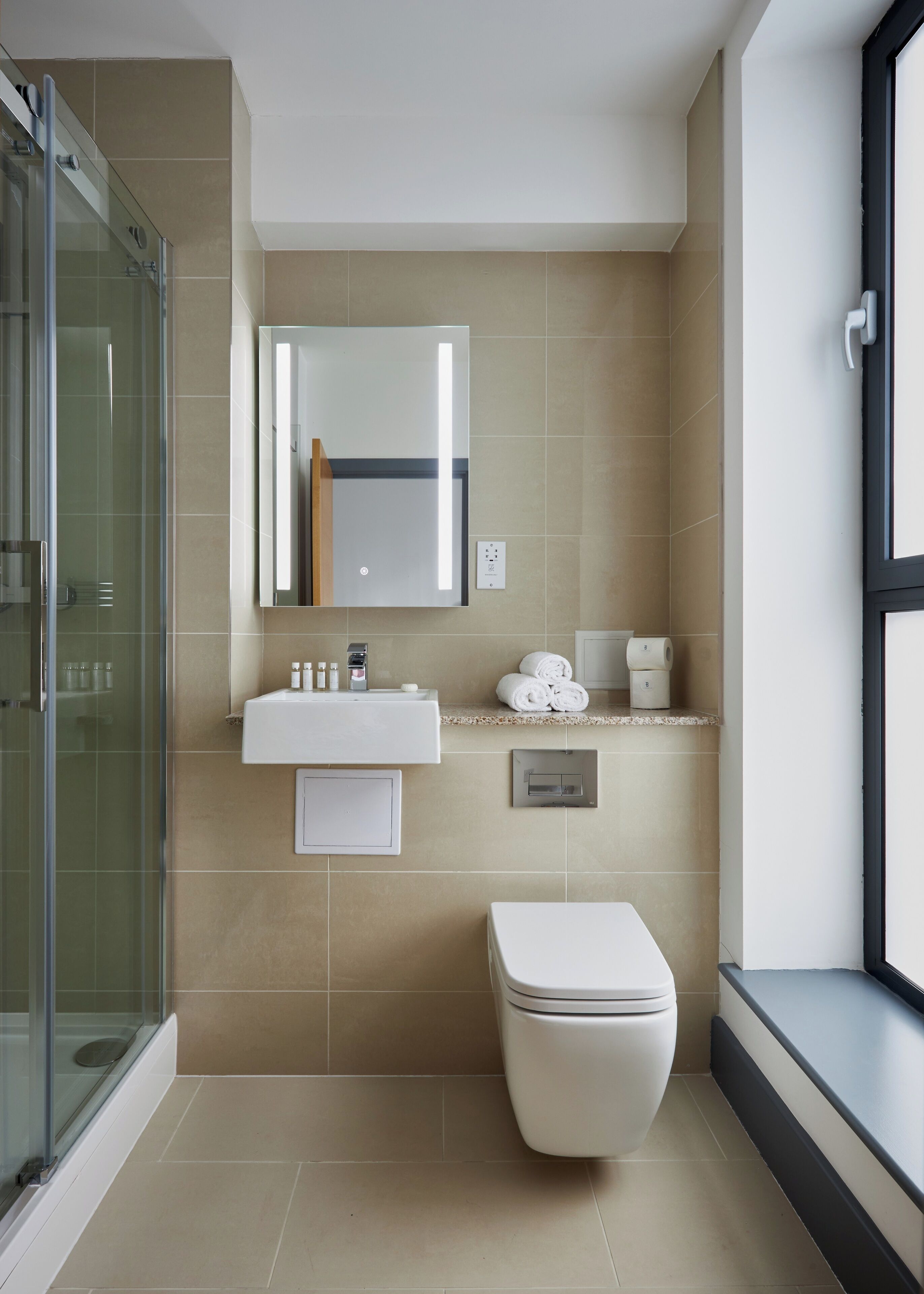 A modern bathroom with a glass shower enclosure, a white sink with toiletries, a toilet, and a large mirror above the sink.