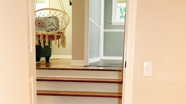 Una escalera de madera con peldaños y apoyabrazos blancos, que lleva a un cuarto con una silla colgante.