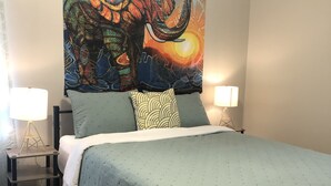Un dormitorio con una cama, un tapiz, dos lámparas de noche y una mesita.