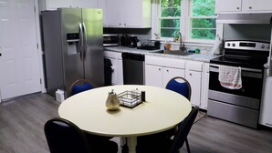 Una cocina compacta con armarios blancos, electrodomésticos de acero inoxidable y una mesa de comedor redonda con sillas azules.