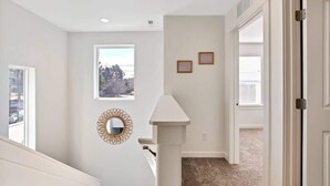 A hallway with a white wall, a window, a mirror, and a door.