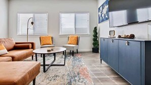 A living room with a sofa, two armchairs, a coffee table, a cabinet, and a television.