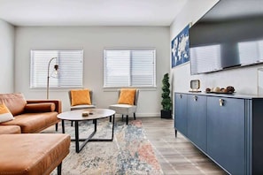 A living room with a sofa, two armchairs, a coffee table, a cabinet, and a television.