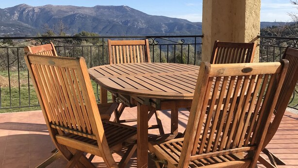 Ein Holztisch mit Stühlen auf einer Terrasse, mit Blick auf die Berge.