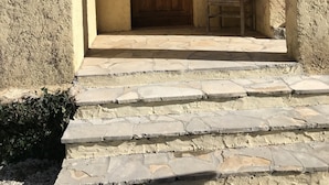 Eine steile Steintreppe führt zu einer Holztür mit einem Metallgriff und einem kleinen Fenster darüber.